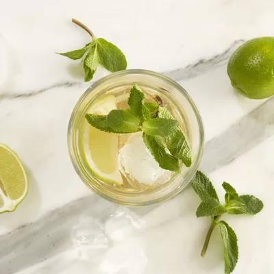 Inquadratura dall’alto di cocktail al lime e menta visto dall'alto, servito in un bicchiere con ghiaccio, agrumi o erbe aromatiche visibili accanto.