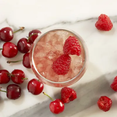 Primo piano di cocktail rosa con agrumi e ciliegie, servito in un bicchiere o in una coppa con ingredienti decorativi e luce morbida.