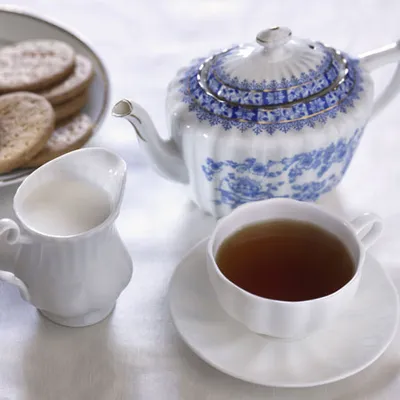 Primo piano di tazza di tè con teiera blu decorata, ripresa su tavolo o sfondo neutro con attenzione ai dettagli del servizio da tè.