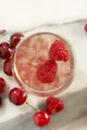 Primo piano di cocktail rosa con agrumi e ciliegie, servito in un bicchiere o in una coppa con ingredienti decorativi e luce morbida.