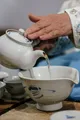 Persona che versa il tè da una teiera bianca dentro tazze o ciotole, in una scena di degustazione ravvicinata.