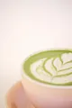 Matcha latte caldo in una tazza rosa, con schiuma di latte decorata a forma di foglia.