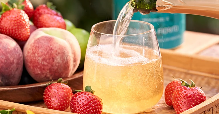Bevanda alla frutta servita in un bicchiere, con barattolo di tè in primo piano e frutta fresca disposta intorno.