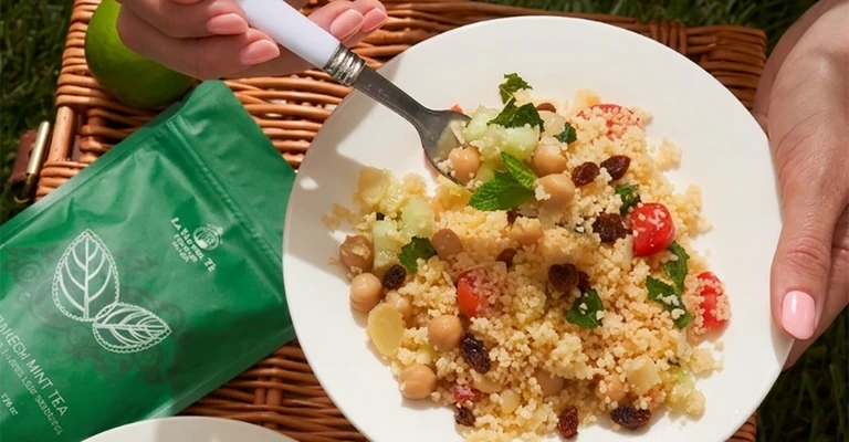 Scena di picnic all’aperto con picnic con piatto di pasta e borsa verde, piatti e accessori disposti su una tovaglia o sul prato.