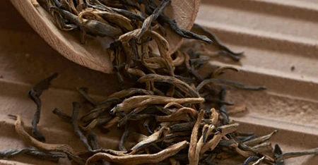 Primo piano di foglie di tè arrotolate che escono da un cesto, ripreso da vicino per mostrarne consistenza, colore e forma su fondo chiaro o naturale.