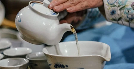Persona che versa il tè da una teiera bianca dentro tazze o ciotole, in una scena di degustazione ravvicinata.