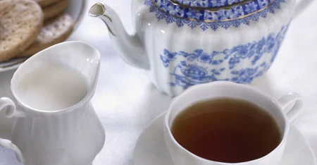 Primo piano di tazza di tè con teiera blu decorata, ripresa su tavolo o sfondo neutro con attenzione ai dettagli del servizio da tè.